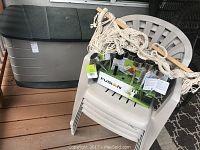 Four beige plastic stacking deck chairs with large black and gray storage bin behind, hammock resting on chairs, box of Fusion solar garden lights on chair seat.