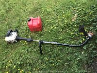 Photo showing Ryobi 31cc gas powered weed eater with black handle and curved shaft, placed on grass next to a small red gas can.