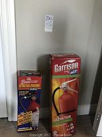 Photo showing two fire extinguisher boxes side by side against a white wall, Garrison on the right and Pyrene Plus on the left.