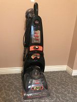 Full view of the upright carpet cleaner showing the handle, body with control buttons, and clear water tank.