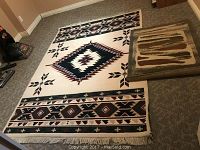 Large Navajo style area rug laid out flat showing full pattern and fringed edges alongside smaller doorway mat with stripes