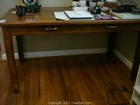 Angle showing the full wooden desk with two drawers, visible wear and marks on legs and surface.