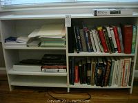 White wooden bookshelf filled with books and stacks of paper and writing pads on multiple shelves
