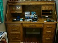Front view of wooden roll-top desk displaying its drawers, sliding cover, and various objects on desktop.