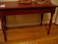 Full view of the red wooden table showing rectangular top and turned legs on wooden floor.