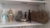 Shelf with various Asian decorative items including two vases, ceramic owl, wooden statues, bowl with saucer, and clay boat figurine