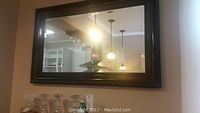 Full view of the rectangular beveled mirror mounted on wall reflecting kitchen and hanging pendant lights.