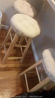 Top and side view of three light wood bar stools with white round cushioned seats with visible tufting, showing the legs and support bars.