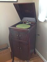 Front view with hinged lid open showing turntable, tonearm, green felt mat, side crank and manufacturer decal inside lid