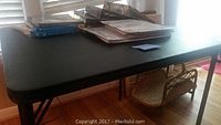 Black card table with books and photo albums on top by window, wooden floor