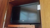 Front view of the Sanyo flat-screen TV with black frame on wooden shelving.