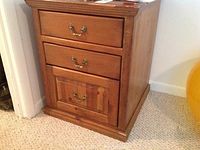 Front view of brown wooden end table showing three drawers and metal handles, with visible wear and scratches.