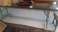 Full view of a brown rectangular folding table supported on metal legs with some items placed on top.