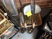 View of two fishing rods with cork handles and black fly fishing reels, attached fishing line, beside tackle boxes and coolers