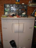 Full view of beige plastic cabinet with two front doors and multiple transparent drawers on top, showing wear and some attached black holder.