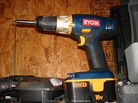 Blue and black Ryobi ONE+ 18V cordless drill with battery and charger on wood surface