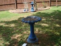 Blue painted concrete bird bath with scalloped top edge and pedestal base on grass.