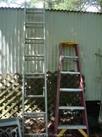 Two ladders side by side outdoors against a corrugated metal wall: a red Werner 5-step ladder with yellow platform and a taller metal extension ladder with aluminum finish.