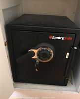 Closed view of the black Sentry Safe showing combination dial, handle, key lock, and brand logo.