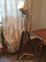 Full view of floor lamp showing metal spotlight head on wooden tripod base