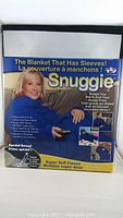 Photo of unopened brand new blue Snuggie blanket with sleeves in original packaging showing features and branding.