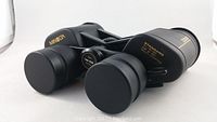 Close-up of black Minolta binoculars with lens caps on and gold lettering showing specifications.
