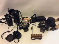 Two camera bodies, lens cases, wooden handle, flash and caps on tabletop