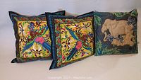 Three decorative throw pillows laid out side-by-side, two with colorful bird designs and one with sheep motif.