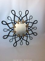 Front view of round Bombay metal wall mirror showing black looping metal frame and gold leaf accents around central mirror glass.