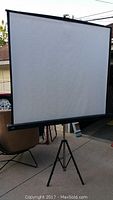 Front view of the 5' x 5' Bretford portable projection screen set on a tripod stand outdoors.