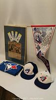 Wide shot of all memorabilia items including two hats, pennant, folded T-shirt, and framed tickets