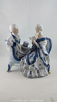 Porcelain figurine group of Victorian couple reading, front and side views showcasing blue and white floral patterns and gold accents on figurine base.