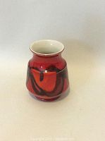 Small red and black ceramic vase with a flared rim, shown on a light neutral background.