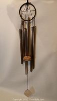 Full view of 45-inch tall wind chime showing the metal tubes, wooden striker, and wind catcher hanging against a plain wall.