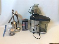 Shows all items in the lot: electric juicer with transparent juice container and pulp compartment, stainless steel hand juice press with lever, and extra Bodum glass juice container in a plastic bag.