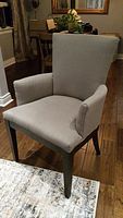 Side angle of the grey upholstered wingback chair showing armrest and seat detail on wooden floor.