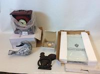 Wooden mantle clock covered in bubble wrap, glass bird figurine in front, iron rooster door knocker to side, mirror serving tray in foam packaging alongside small clock key box.