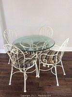 Front view of round glass top kitchen table with four metal chairs with plaid cushions.