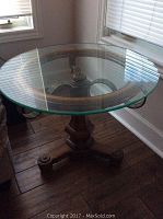 Angle view of round glass top on wooden table base near window.