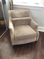 Full front view of beige corduroy accent chair showing cushion and armrests against a white wall and dark hardwood floor.