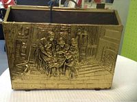 Front and side view of the embossed metal magazine rack showing detailed family scene in embossed relief.