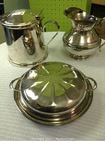 Photo of silverplated ice bucket, pitcher, and covered serving dish on white textured surface.