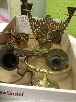 Photo showing brass candlesticks, decorative candle holder, towel holder, and door knob in a box