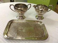 The full set of silver plate cream pitcher, sugar bowl, and tray shown on a textured white surface.