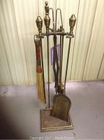 Full view of 6 piece brass-colored fireplace tool set with stand, showing tools hanging and condition details