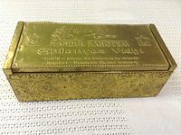 Top and front view of rectangular hammered copper religious box showing embossed text and decorative temple and floral patterns.