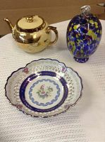 Photo showing all three items: gold Gibson & Son teapot, multicolored art glass piece, Limoges floral bowl on white fabric.