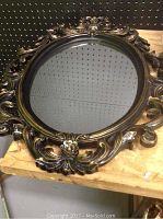 Oval wall mirror showing the entire reflective surface and ornate black and gold plastic frame with scroll and floral designs.