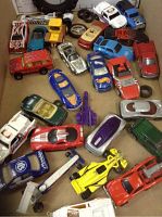 Collection of 26 assorted collectible model cars laid out on a surface, showing a variety of colors and some spare rubber tires.