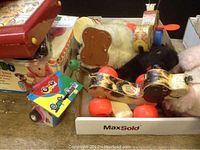 Photo of vintage toys including a small pull toy with colorful wheels, plush animals, and wooden pull toys in a box